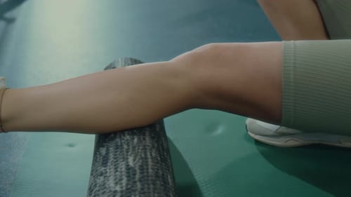 Close Up of Woman Foam Rolling Calves on Gym Floor
