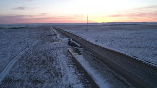 Vue aérienne d'une route interurbaine entourée de champs enneigés au coucher du soleil, paysage hivernal