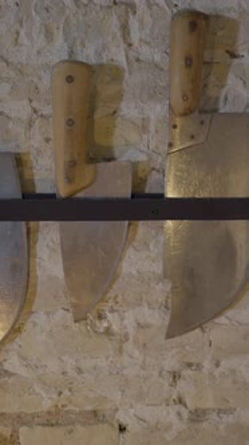 Pushout of Large Knives Hanging By Light Brick Wall in Restaurant