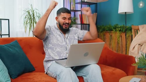 Man Cheers Using Laptop on Orange Couch