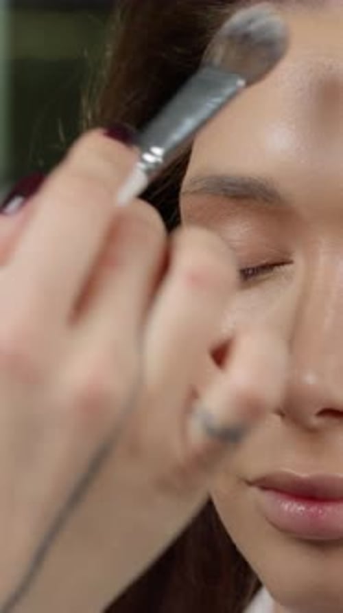 Professional Makeup Artist Applying Silky Foundation on Model's Face Using Specialized Brush