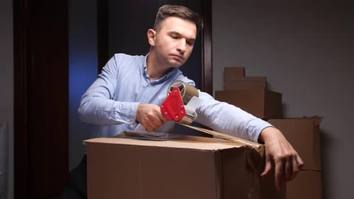 Man Packing Cardboard Box with Tape Dispenser