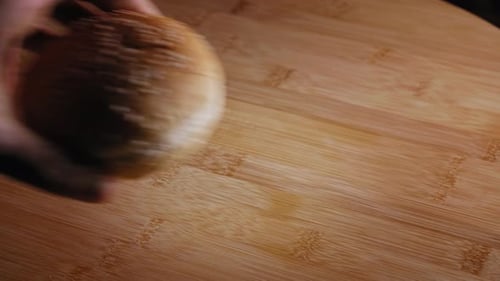 Hand Puts Burger Bun With Sesame Seeds Onto Wooden Board. close up
