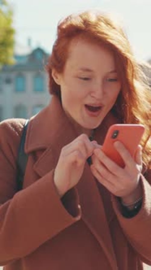 Une femme aux cheveux roux sourit vivement et fiancée avec son smartphone