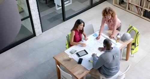 High angle of diverse architects discussing blueprints on table in office, copy space, slow motion