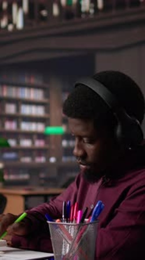 Vertical Video Male Student Listening to Ambient Study Music on Headset and Collecting Data