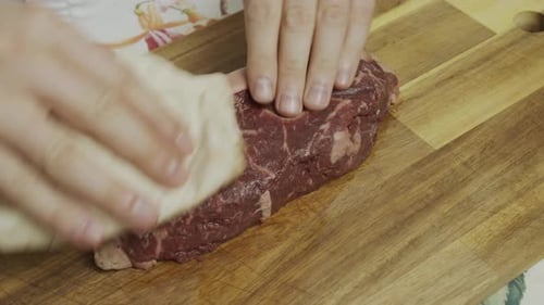 Removing water from meat steak with tissues on the cutting board. Close up shot.