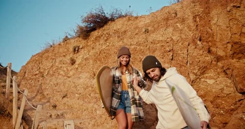Couple Walks on Beach with Surfboards at Sunset