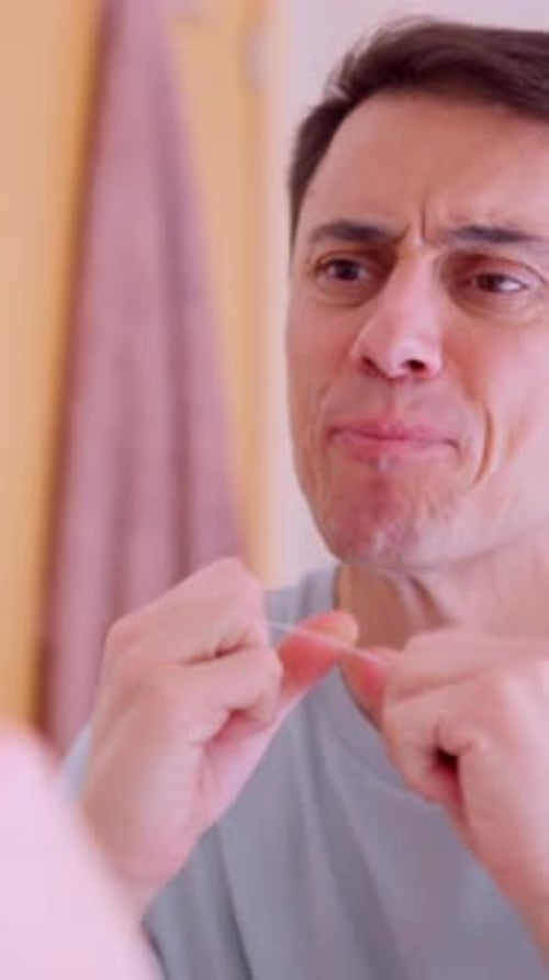 Man Flossing Teeth in Bathroom Mirror