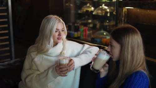 Zwei Frauen auf dem Sofa unterhalten sich entspannt und trinken Cappuccino