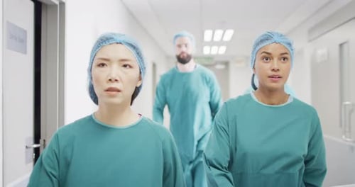 Video of four diverse surgeons in surgical caps and gowns walking in hospital corridor talking