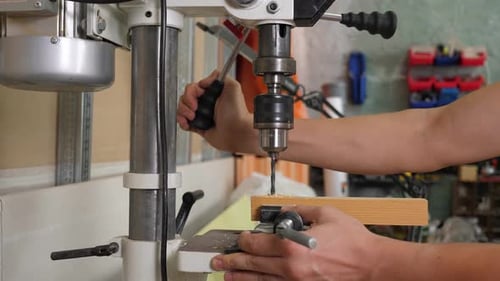 A Carpenter Drilling a Board with an Automatic Drill in a Carpentry Workshop
