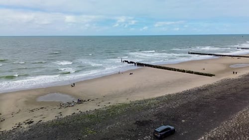 A quiet beach scene with gentle waves wooden breakwaters stretching into the sea few people walking