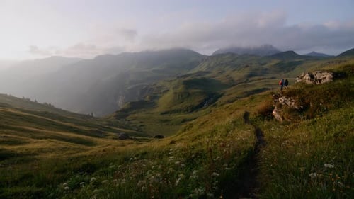 Mountain landscape shot with hikers on trail on the right and sun very low shining from the left