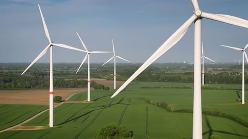 Aerial footage of wind farm with large spinning wind turbines.