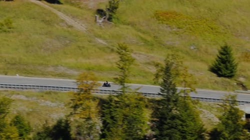 High speed motorcyclist riding along a winding mountain road surrounded by grassy hills and
