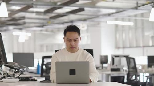 Young businessman working on laptop in modern open plan office portrait