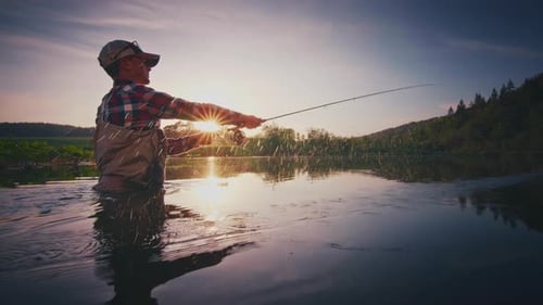Fly fishing. Angler stands in the river and casts the fly at sunset. Fisherman fishing on fly