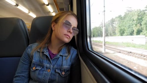 A Tired Woman in Sunglasses is Leaning and Looking Out the Window on the Train