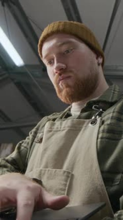 Focused Roaster in Apron and Beanie Typing on Laptop in Coffee Roasting Plant