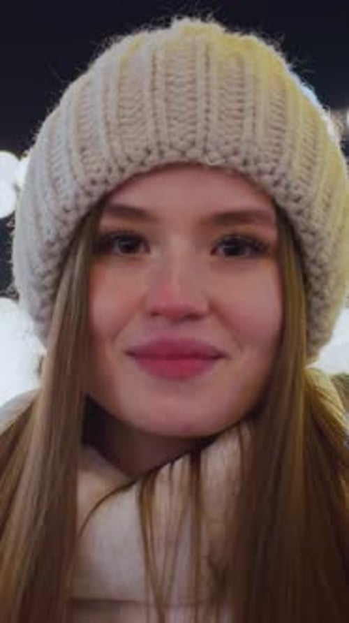Femme souriante en bonnet blanc et veste moelleuse avec lumières festives