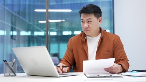 Happy asian businessman satisfied with financial results sitting at workplace in business office.