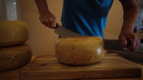 Person Cutting Cheese Wheel on Wooden Cutting Board