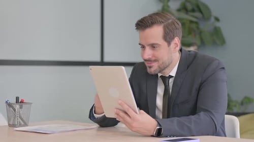 Businessman Using Tablet and Smiling at Desk