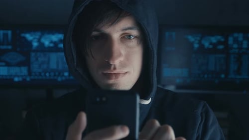 Dangerous Hacker in the Hood Uses a Smartphone in a Secret Data Center Filled with Screens