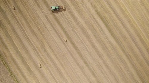 Aerial top down of tractor collecting hay bales of farm field in sunlight,4K