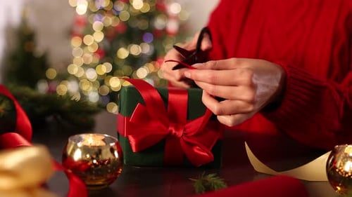 Woman Wrapping Christmas Gift with Red Ribbon