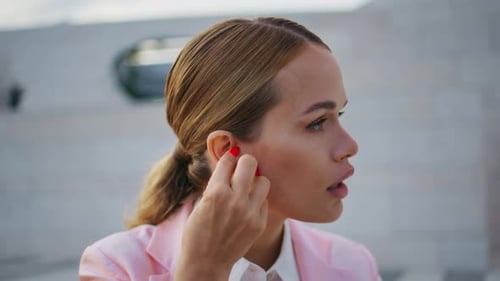 Woman Puts Wireless Headphones in Ear Outdoors