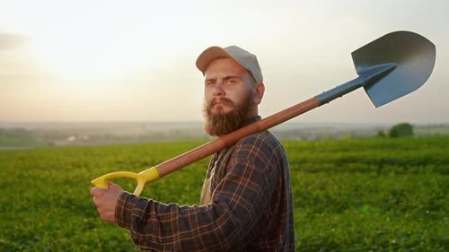 Male Farmer Standing on Field Holding Spade on Shoulder