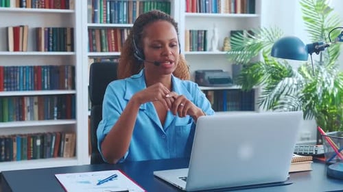 Young African American Woman in Headset for Call Center Sits at Desk with Laptop