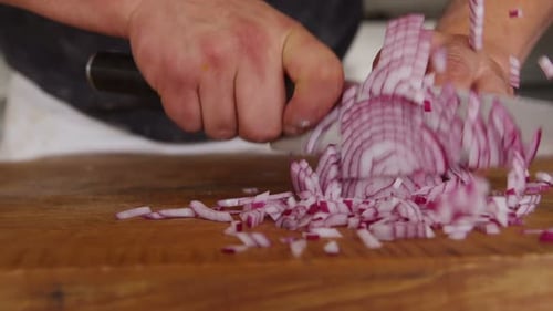 Slow motion close up of a chef chopping a red onion in the kitchen