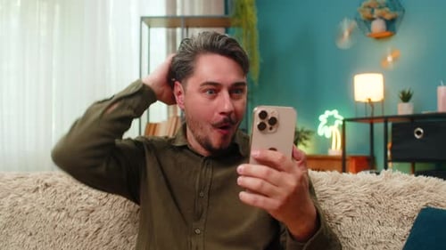 Excited Man Using Smartphone in Modern Living Room