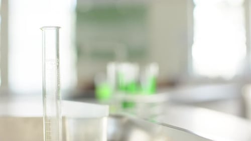 Le focus pull se déplace de la gauche vers le support de tubes à essai, révélant des solutions vert vif pour l'analyse