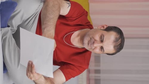 Man Reads Document and Laughs Indoors on Couch