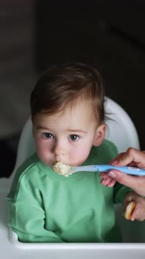 Baby Eating Food with Spoon in High Chair