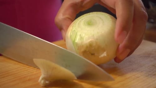Hands Peel Onion on Cutting Board with Knife