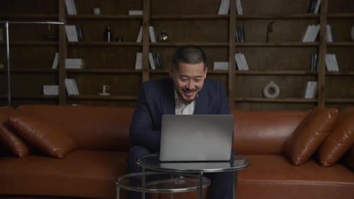 Asian Businessman on a Video Conference Call Using Laptop Computer in His Loft Office