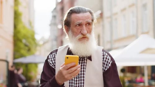Smiling Senior Man Uses Smartphone on City Street