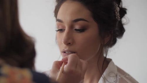 Mixed race bride having her makeup done, specifically her lipstick. Medium-Close shot.