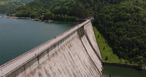 Dam and water reservoir surrounded by green forests, panoramic aerial view. Tracking drone close up
