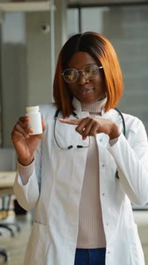 African American Female Doctor in White Coat with Stethoscope in Clinic with Pills