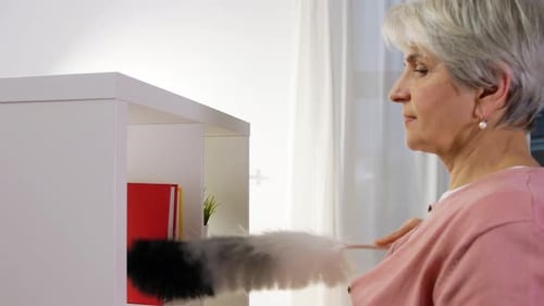 Senior Woman Dusting Shelf in Home Interior
