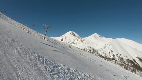 Pista de esquí con telesquí y cima de una montaña al fondo en un día soleado