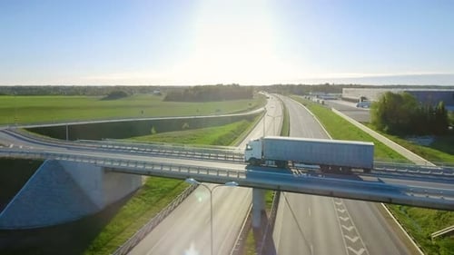 Aerial View of White Semi Truck with Cargo Trailer Passing Highway Overpass/ Bridge. Eighteen Wheel