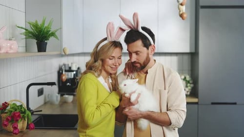 Cheerful Couple Holding a White Rabbit in Kitchen