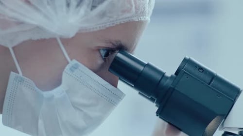 Close-Up of Female Scientist in Protective Mask Looking in Microscope